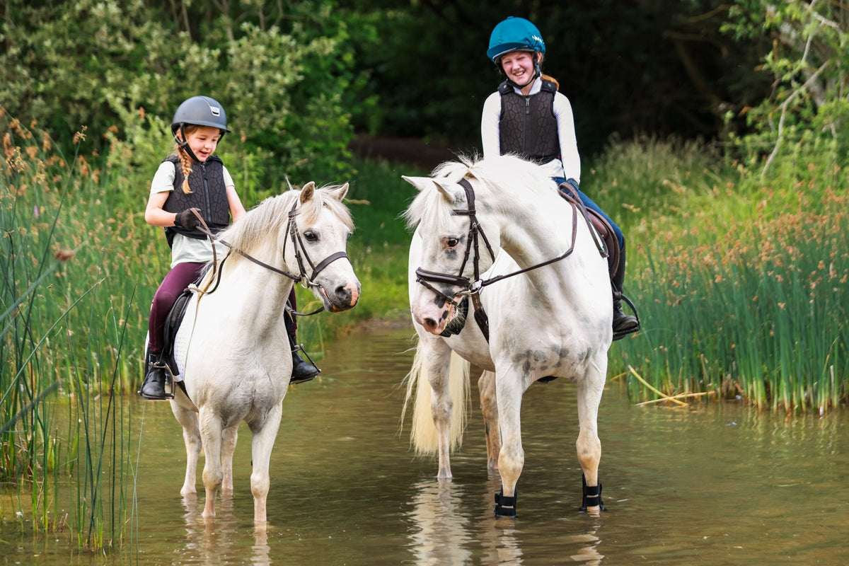 Image of two ponies and riders stood in a river